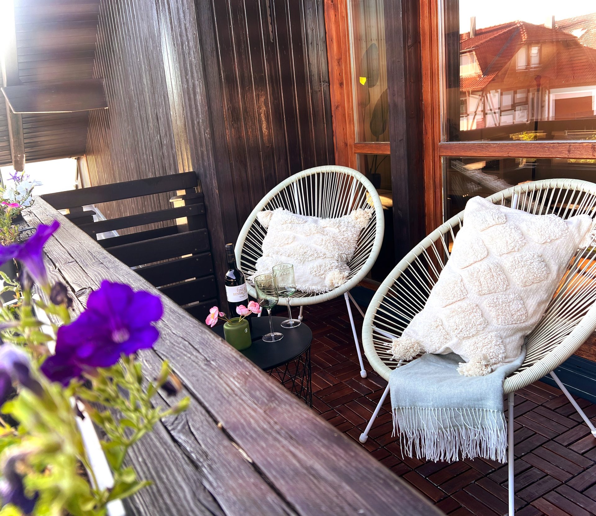 Balkon mit Blumen, zwei weißen Sesseln und einem Glas Wein in der Abendsonne