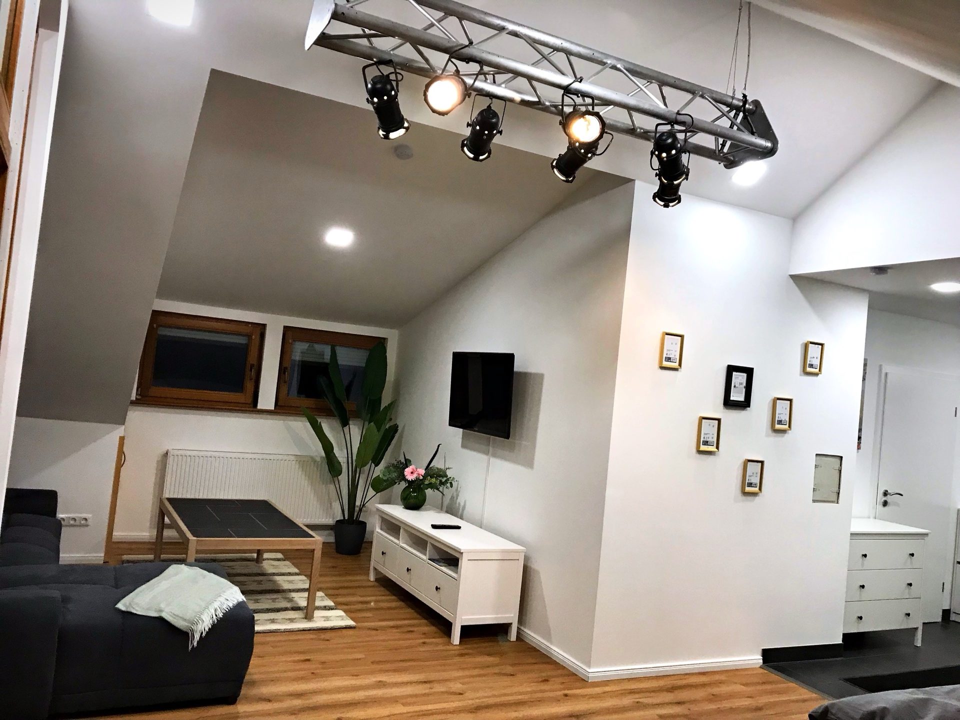 Wohnbereich am Abend mit großer Couch, TV und Strahlern an der Decke